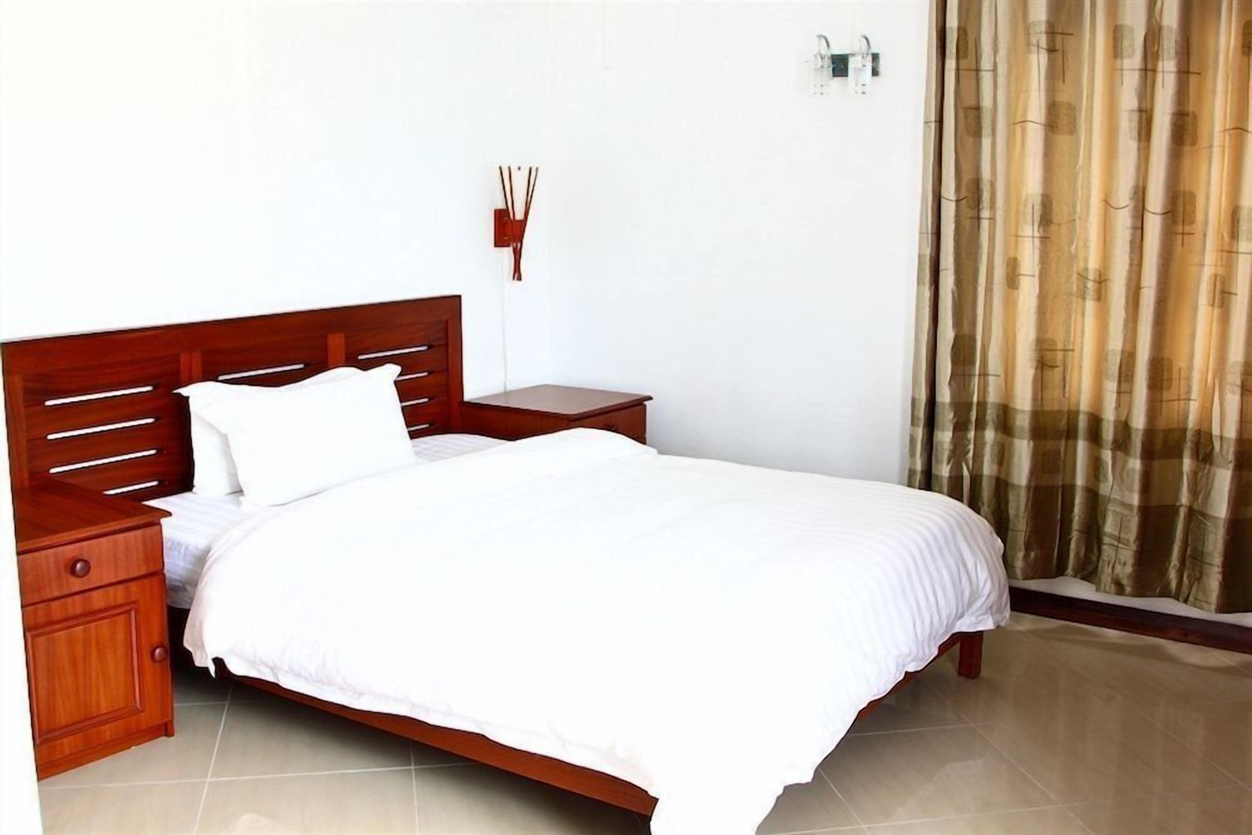 A neatly made bed with a wooden headboard, a bedside table, and a wall-mounted light fixture.