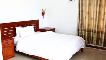 A neatly made bed with a wooden headboard, a bedside table, and a wall-mounted light fixture.