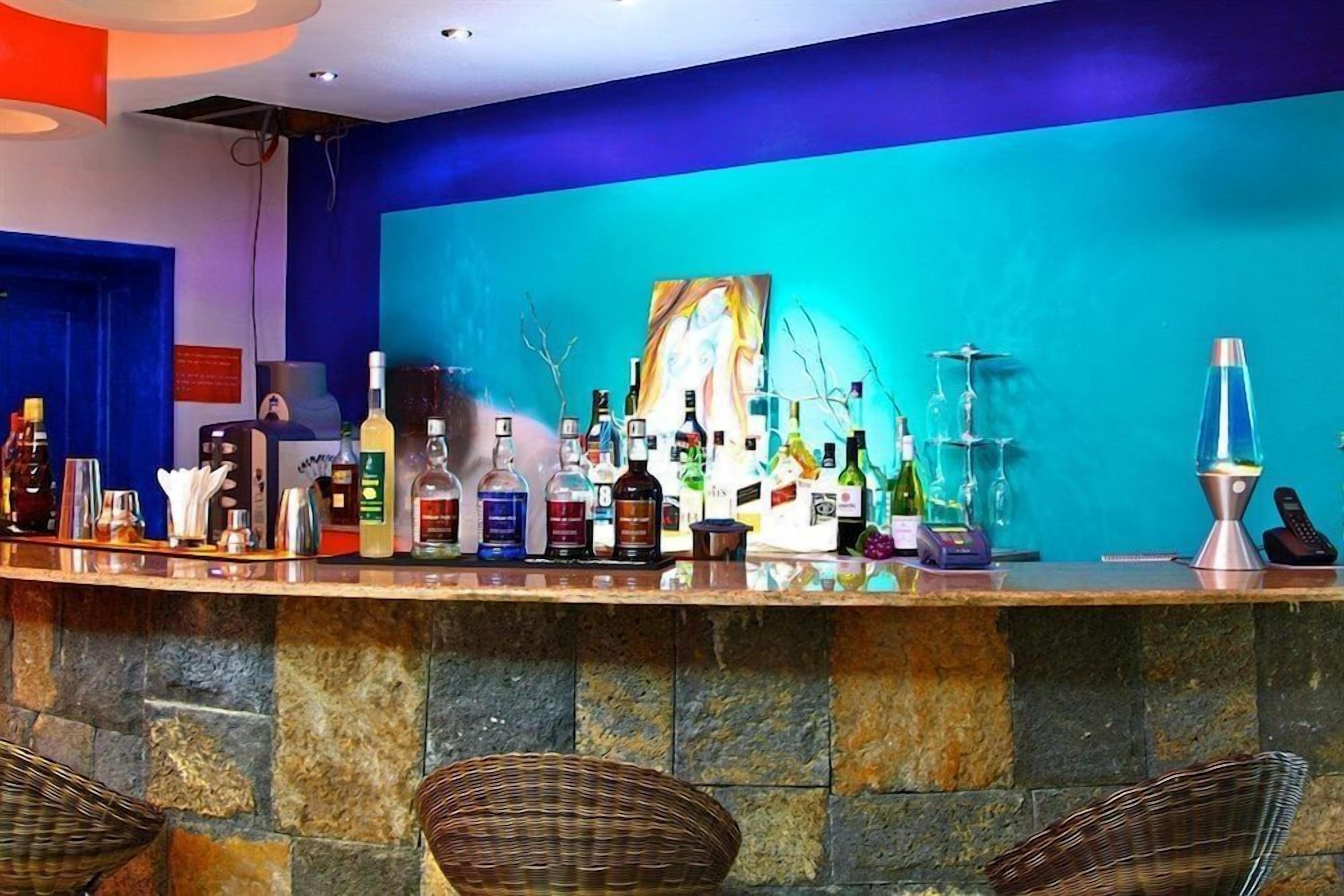 Una zona de bar con una variedad de botellas, un cuadro y una lámpara de lava.