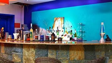 Una zona de bar con una variedad de botellas, un cuadro y una lámpara de lava.