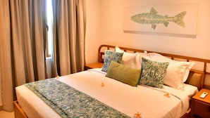 Habitación de hotel con cama, cortinas, un cuadro de un pez colgado en la pared y una mesita de noche con un teléfono.
