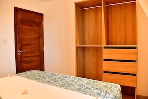 A bedroom with a wooden wardrobe, a bed with a patterned bedspread, and a door. - Orchid Villas Mauritius (Belle Mare)