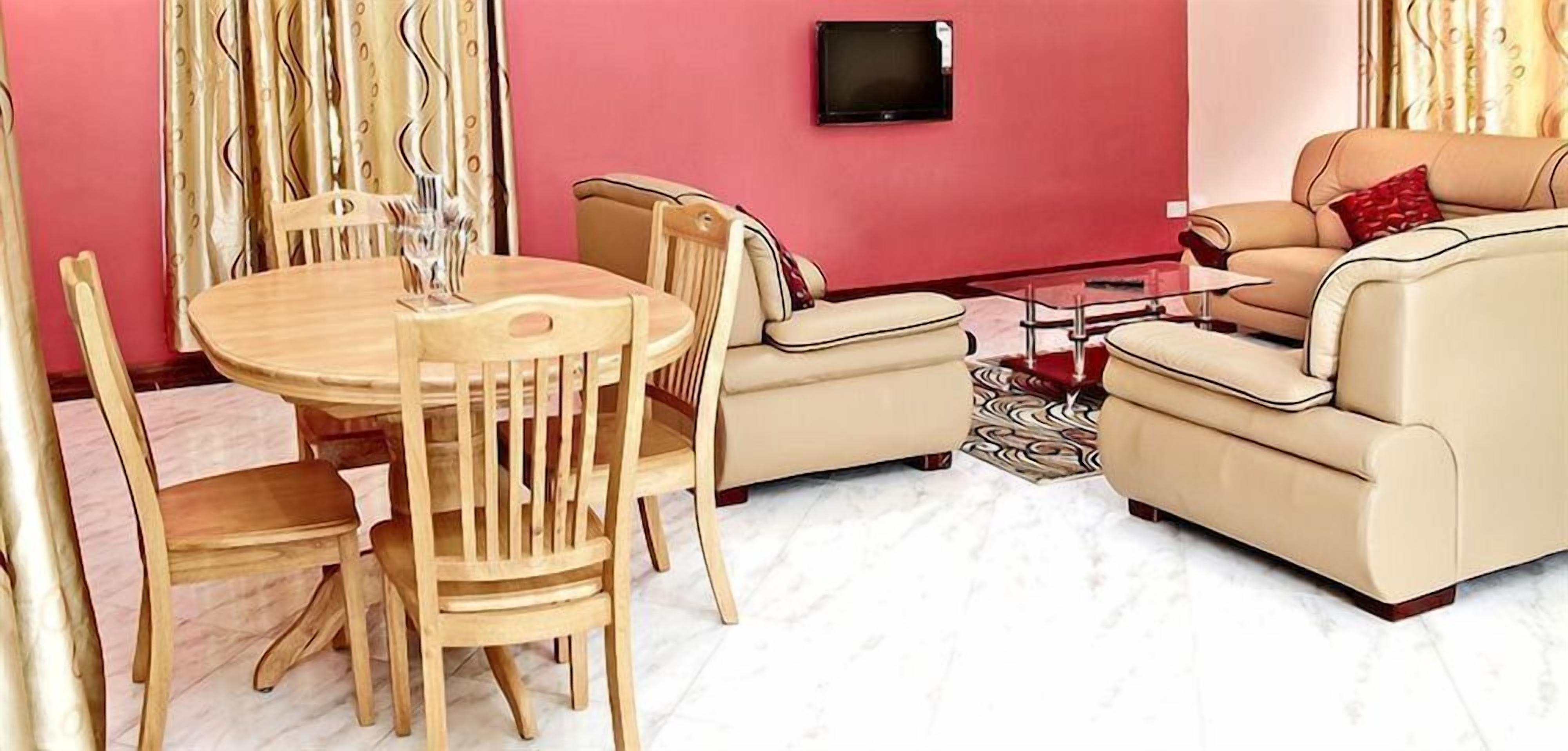Una sala de estar con una mesa redonda de madera, dos sofás color beige y un televisor montado en la pared.