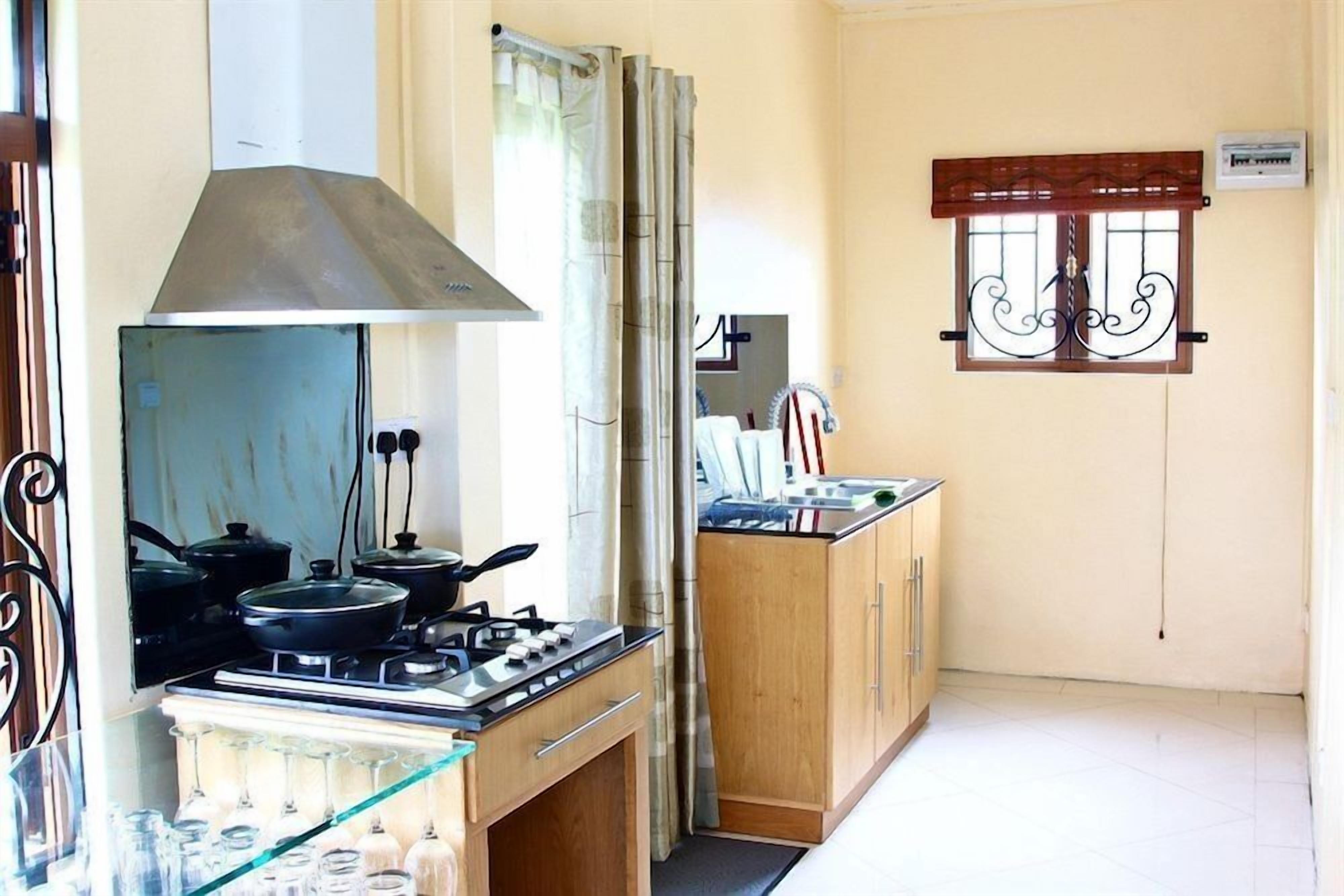 Una cocina compacta con estufa a gas, extractor de humos y ventana con celosías decorativas.