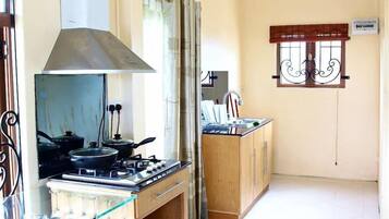 Una cocina compacta con estufa a gas, extractor de humos y ventana con celosías decorativas.