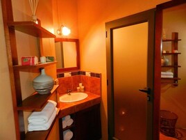Un baño con lavamanos, espejo, repisas con toallas y zona de ducha.