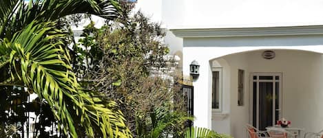 Um edifício branco com um pátio, que inclui móveis de vime branco e uma mesa com um vaso.