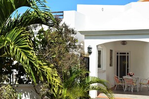 Edificio blanco con un patio amueblado con mobiliario de mimbre blanco y una mesa con un florero.