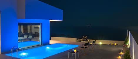 Un área de piscina moderna al aire libre con cerramiento de vidrio, zona de barbacoa y mobiliario.