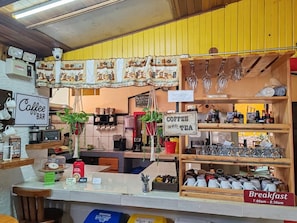 A coffee bar with a sign indicating it serves coffee and tea, and a breakfast sign with hours of operation. - Cabinas El Pueblo B&B (Monteverde)