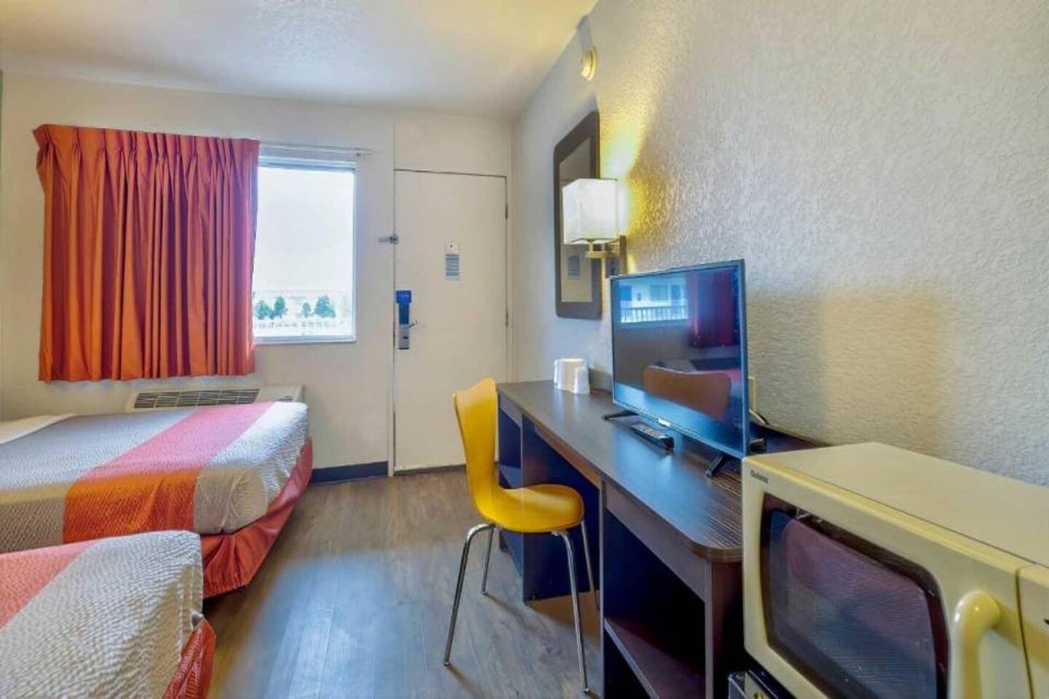 Quarto de hotel com duas camas, uma escrivaninha, uma cadeira, uma televisão e uma janela com cortinas.