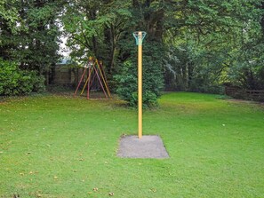 A grassy area with a single yellow pole and a small square base, surrounded by trees and a swing set. - 3 bedroom accommodation in Cockermouth (Cockermouth)