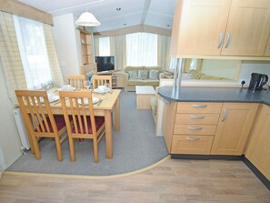 A compact kitchen with wooden cabinets, a dining table with chairs, a sofa, and a television. - 3 bedroom accommodation in Cockermouth (Cockermouth)