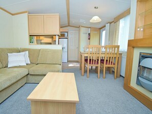 Ein kompakter Wohnraum mit einer Couch, einem Esstisch mit Stühlen, einer Küchenzeile und einem kleinen Fenster.
