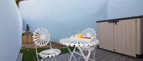 A deck with two white chairs and a table, a white fence, and a wooden deck.