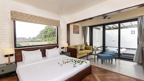 A hotel room with a large bed, a sofa, a small table, and a view of a swimming pool.