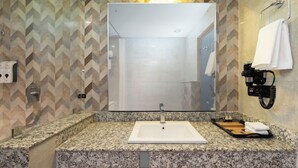 A bathroom with a granite countertop, a white sink, a mirror, and a towel rack.