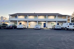 Un motel con una struttura a due piani, un parcheggio con diverse auto e una porta blu al piano terra.