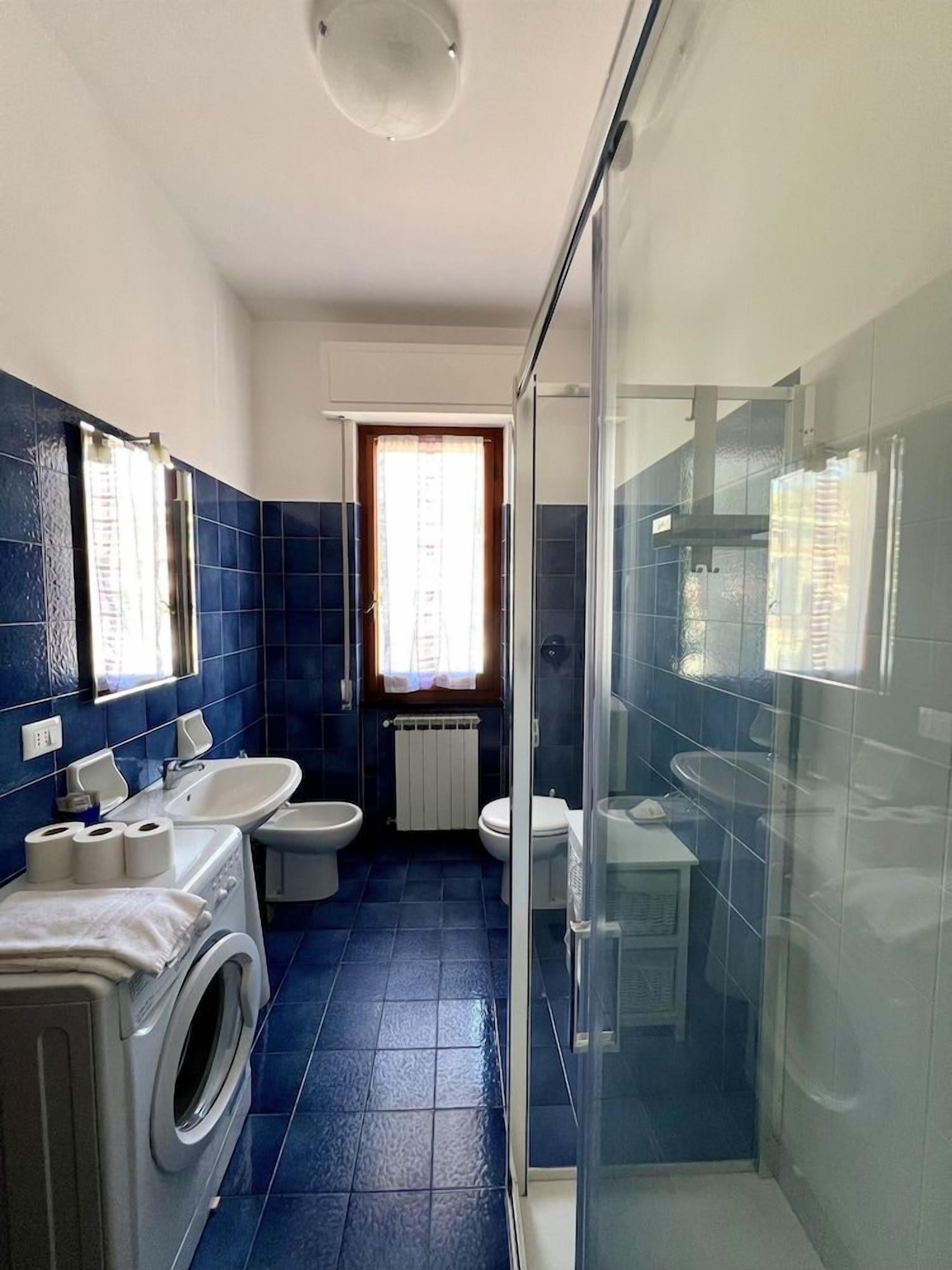 Ein Badezimmer mit Waschmaschine, zwei Waschbecken, einem Bidet und einer Duschkabine.