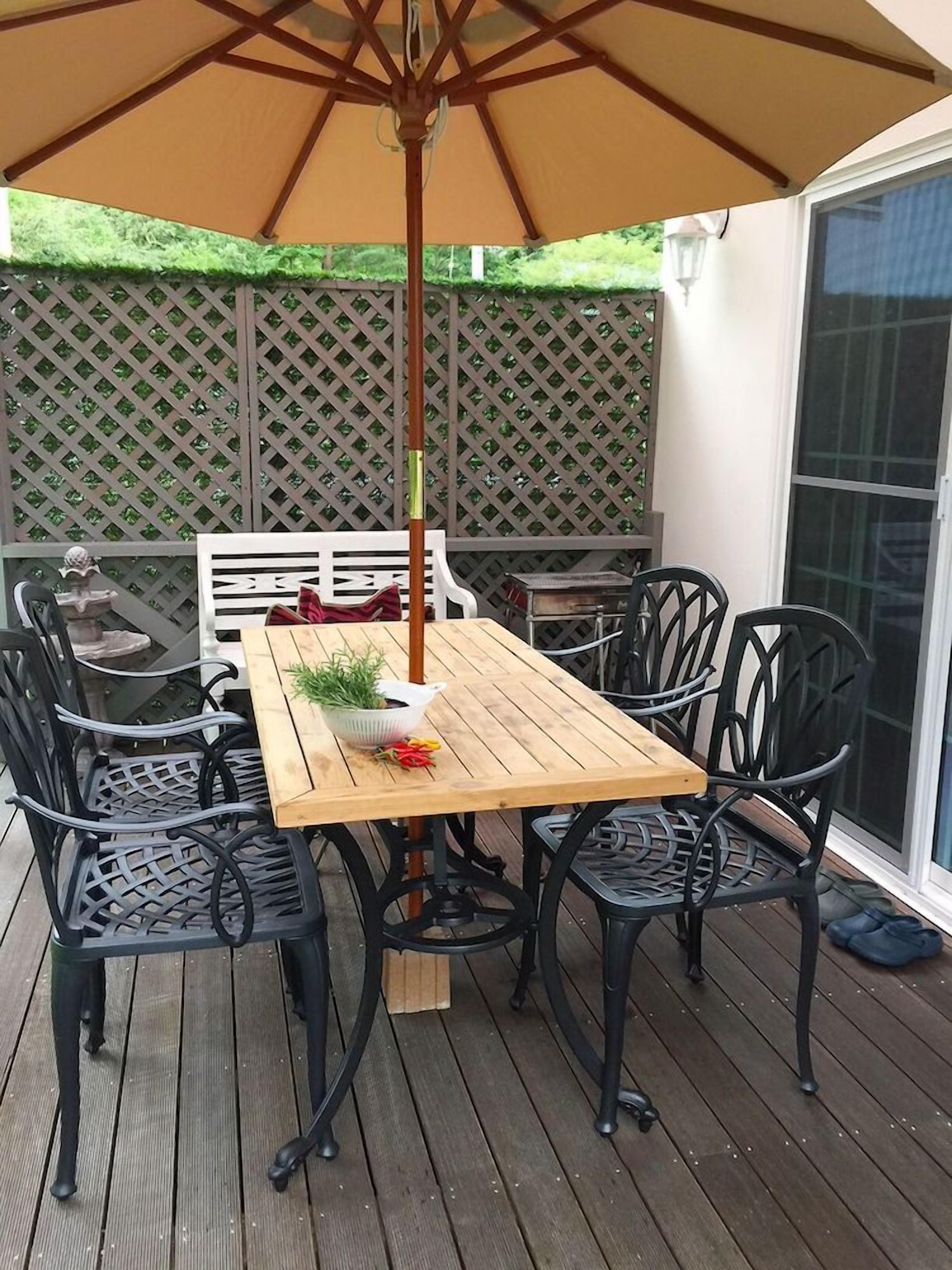 An outdoor patio with a wooden table and chairs, an umbrella, and a lattice fence.