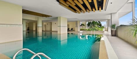 An indoor swimming pool with clear water, a metal ladder, and a ceiling with wooden beams.