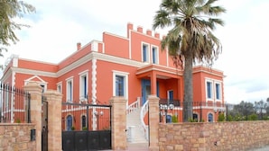 A large, two-story building with a red facade, a stone wall, and a palm tree. - Villa Rossa Kambos (Chios)