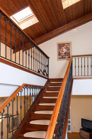 Una scala in legno con ringhiera in metallo nero, un lucernario e un quadro appeso al muro.