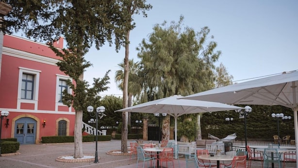 An outdoor patio area with tables and chairs, a covered seating area, and a building with a red facade. - Villa Rossa Kambos (Chios)