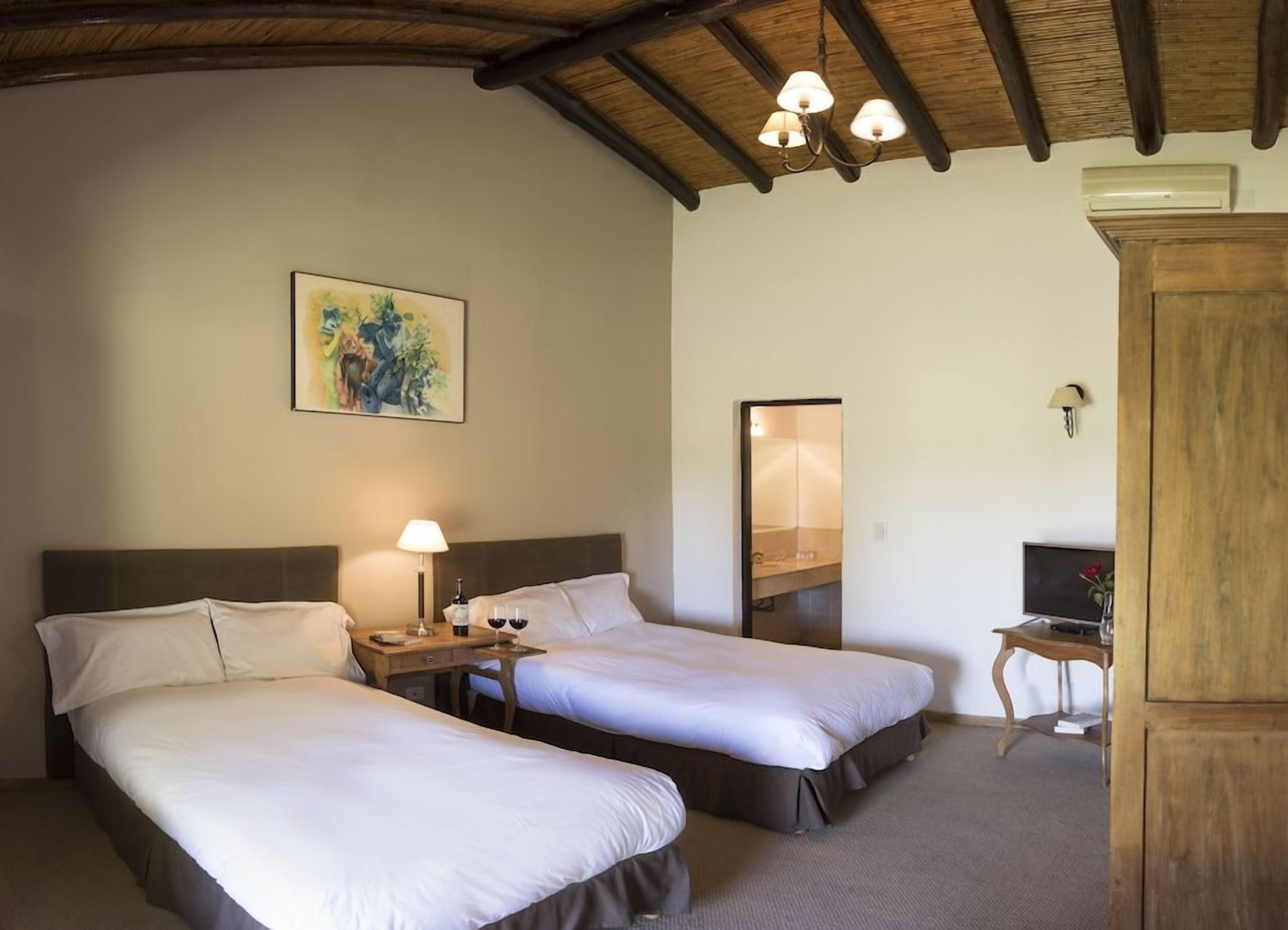 A hotel room with two beds, a nightstand with a lamp, a painting on the wall, and a wooden cabinet.