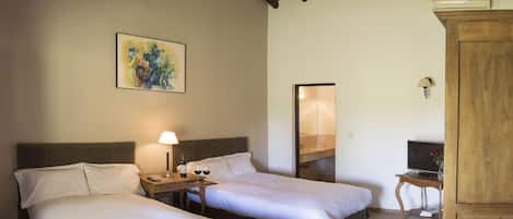 Une chambre d’hôtel avec deux lits, une table de chevet avec une lampe, un tableau au mur et une armoire en bois.