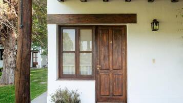 Un edificio blanco con puerta y ventana de madera, una maceta con plantas y un farol en la pared.