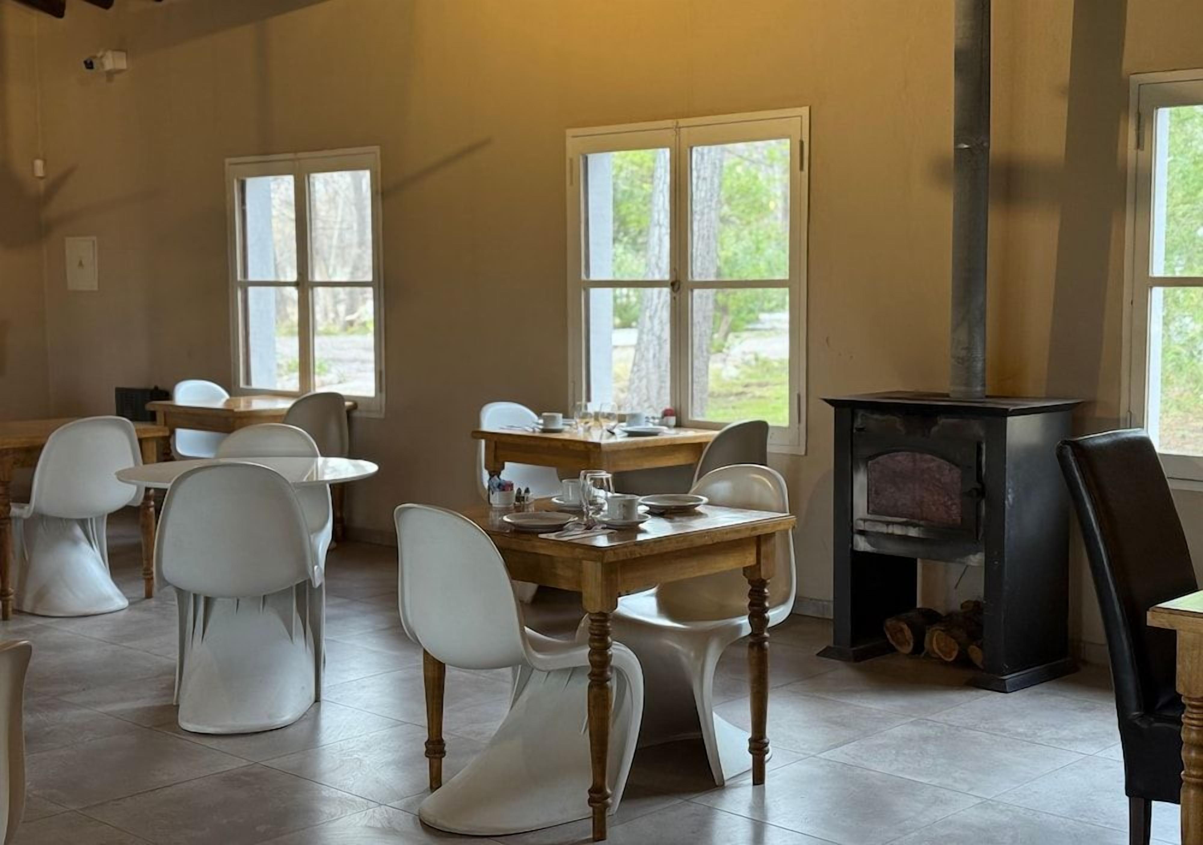 A dining area with a wooden table and white chairs, a fireplace, and large windows.