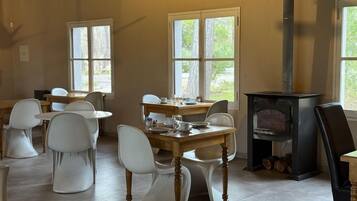 A dining area with a wooden table and white chairs, a fireplace, and large windows.
