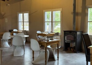 Un espace repas avec une table en bois et des chaises blanches, une cheminée et de grandes fenêtres.