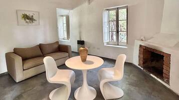 A living room with a brown sofa, two white chairs, a round table, a fireplace, and a window.