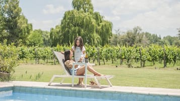 A poolside area with a lounge chair and a table, surrounded by a vineyard.