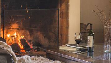 A cozy living room with a fireplace, a glass of wine, a book, and a bottle of wine on a wooden table.