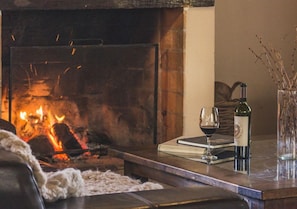 A cozy living room with a fireplace, a glass of wine, a book, and a bottle of wine on a wooden table. - Postales Hotel Boutique Valle del Uco (Tunuyan)