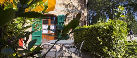 Un espace extérieur aménagé avec une table et des chaises, un pot de fleurs et un bâtiment doté d’une façade en pierre et de volets verts.