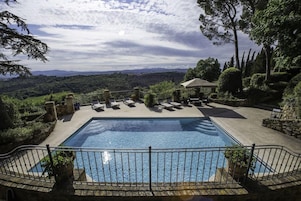 Una piscina rectangular con un deck perimetral, un muro de piedra y vistas a un paisaje montañoso.