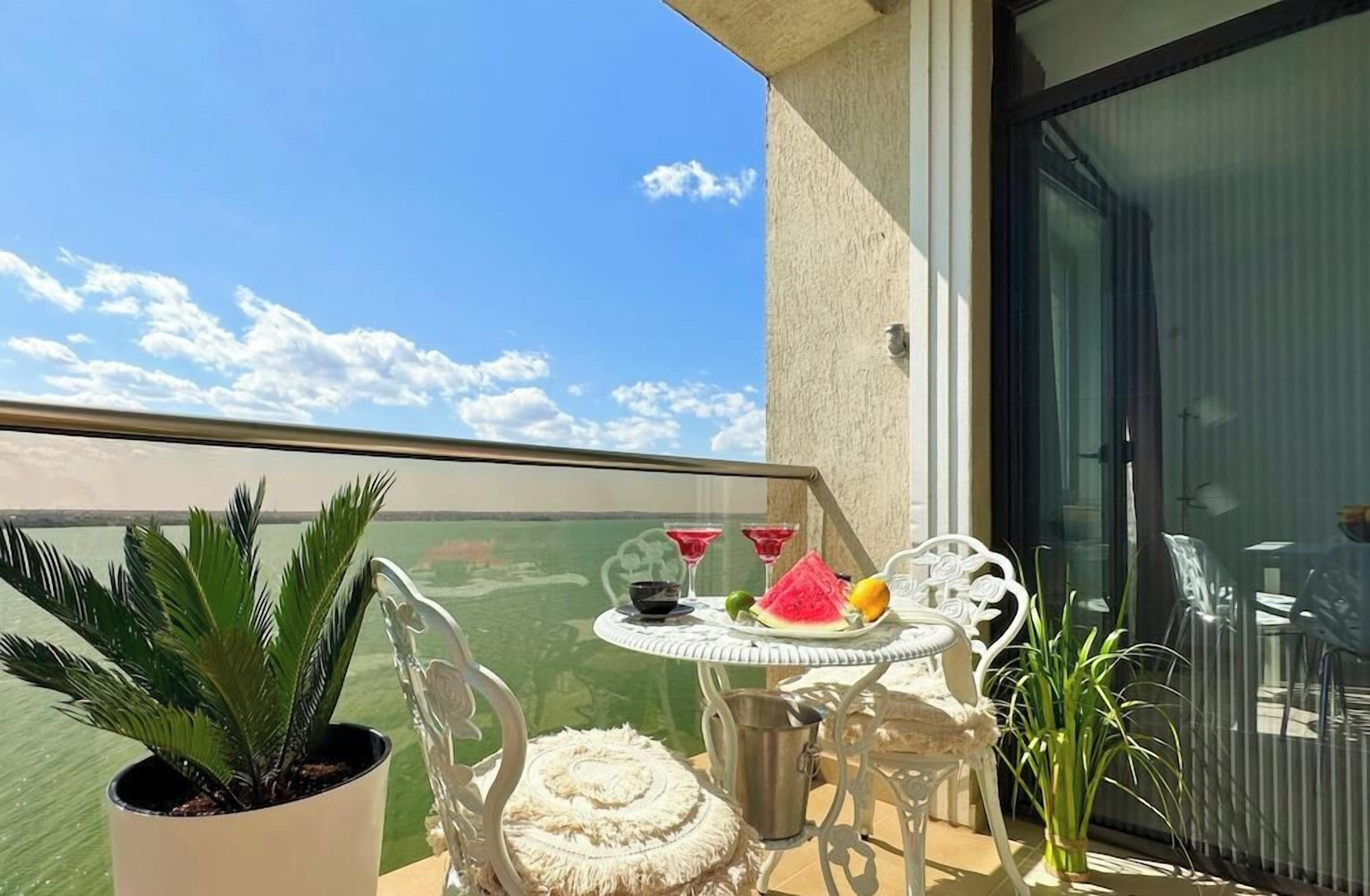 A balcony with a table set for two, a potted plant, and a view of the sea.