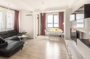 A modern living room with a sofa, dining table, and chairs, a TV, and a view of the outdoors. - Deluxe Nicolle Solid Residence Mamaia (Constanta)