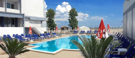 A pool area with blue lounge chairs, red umbrellas, and potted plants.