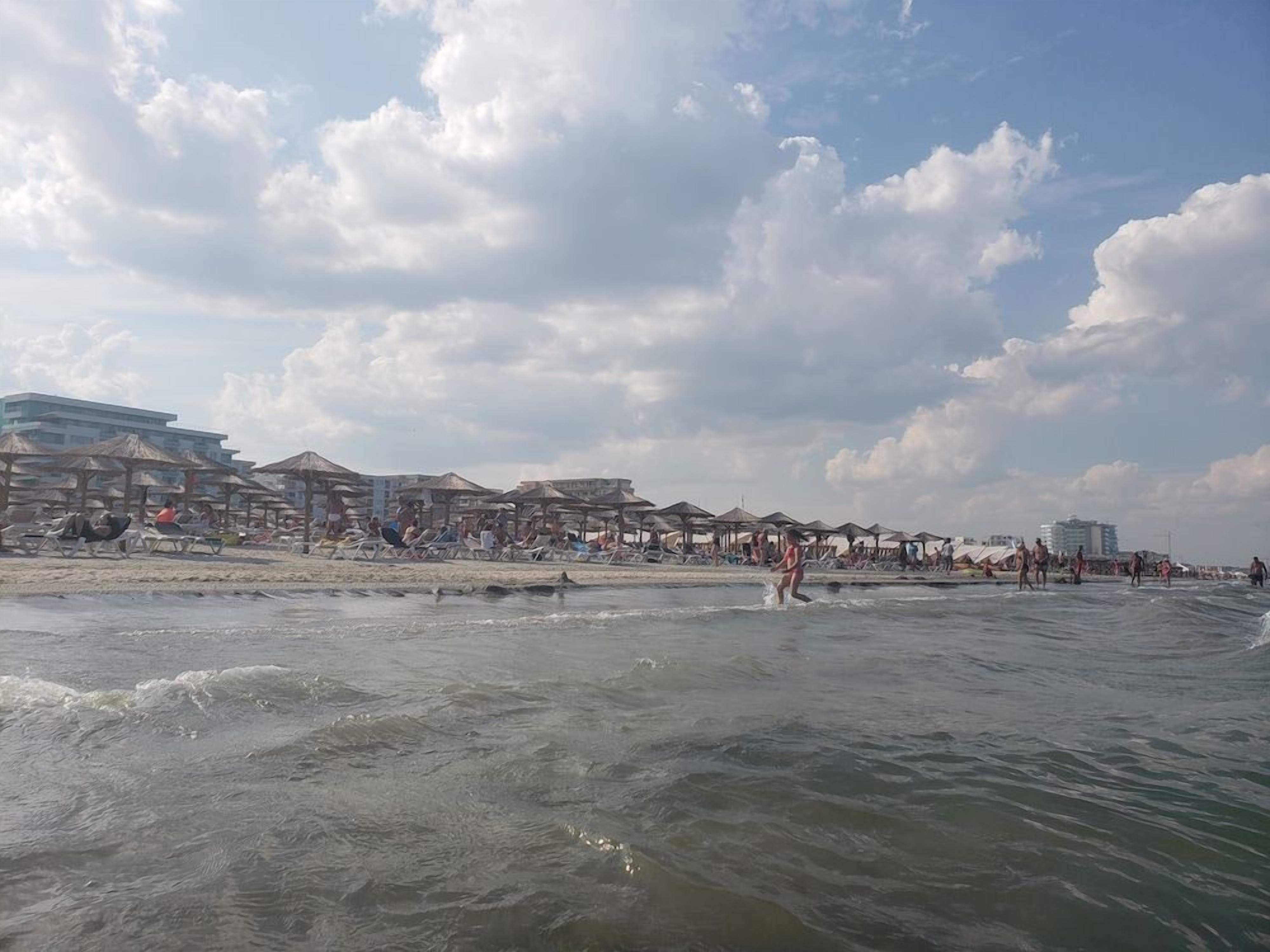 A beach with umbrellas and people, a building with multiple floors, and a clear sky.