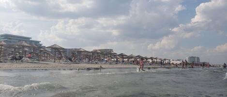 A beach with umbrellas and people, a building with multiple floors, and a clear sky.