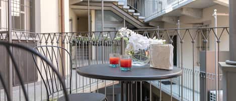 A balcony with a round table, two chairs, a vase with white flowers, and two glasses of red drink.