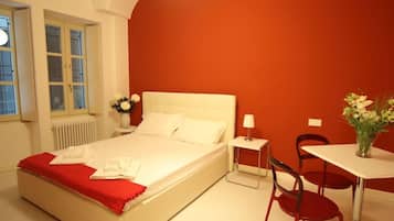 Una camera d'albergo con un letto, un tavolino, due sedie, una finestra e un termosifone.