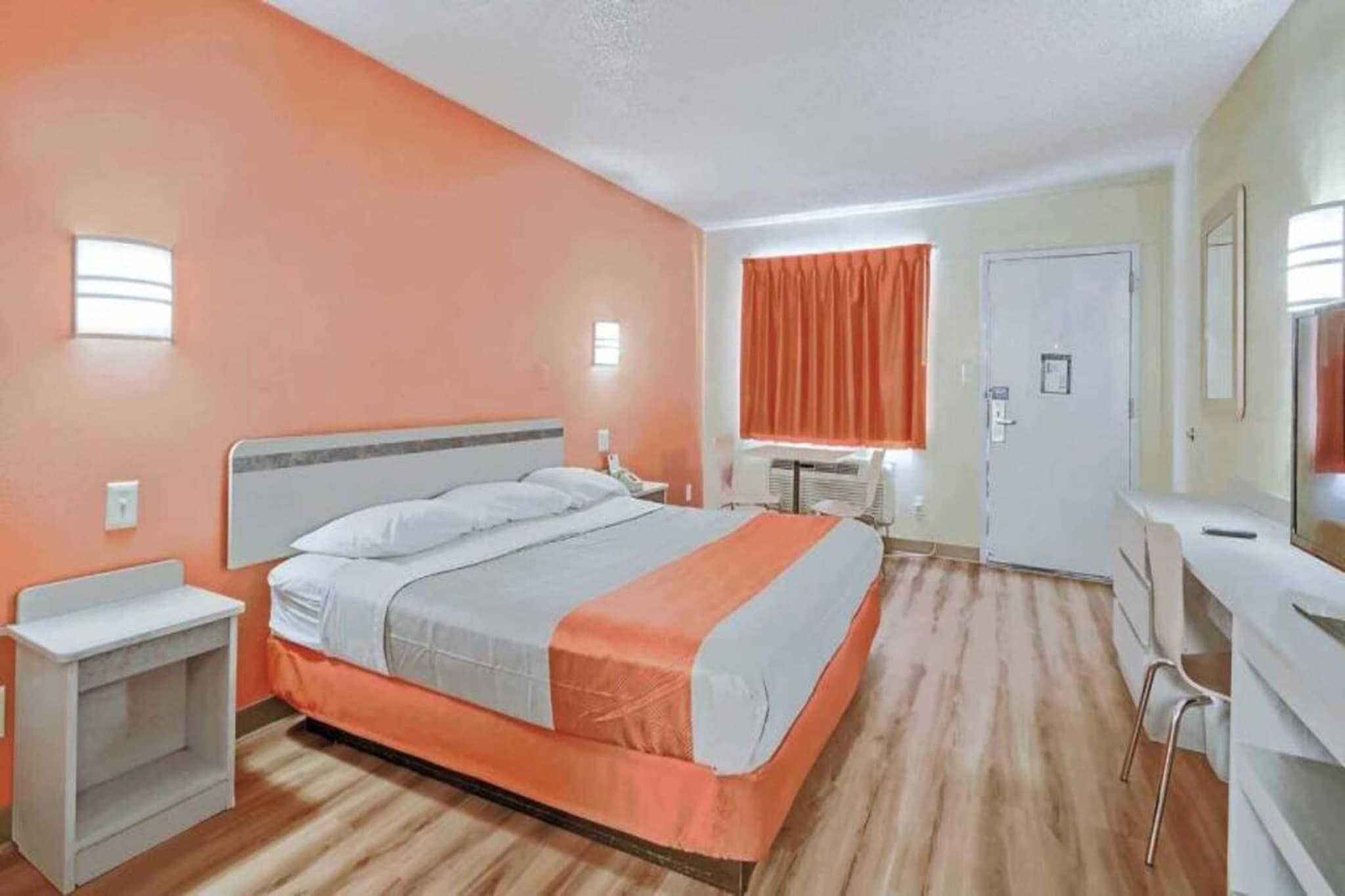 Een hotelkamer met een bed, nachtkastje, bureau, stoel en een raam met gordijnen.