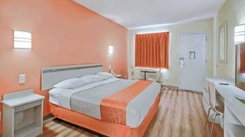 Een hotelkamer met een bed, nachtkastje, bureau, stoel en een raam met gordijnen.