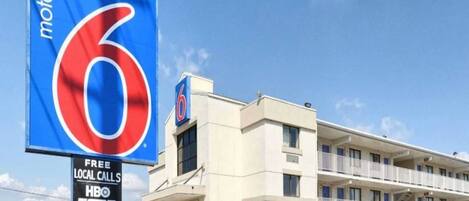A motel with a large blue sign featuring the number 6 and a smaller sign advertising free local calls, HBO, ESPN, and more.